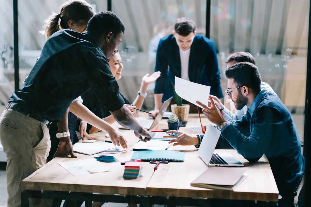 A group discussion takes place around a table in an office workspace.