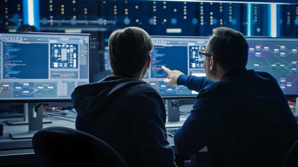 Two Professional IT Programers Discussing Blockchain Data Network Architecture Design and Development Shown on Desktop Computer Display. Working Data Center Technical Department with Server Racks