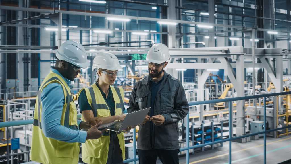 Young Diverse Team of Car Factory Specialists Working on Laptop and Tablet Computers. Engineers Discussing Automotive Industrial Manufacturing Technology on Modern Vehicle Assembly Plant.