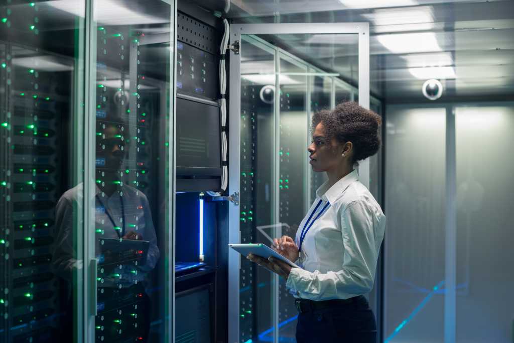 Medium shot of female technician working on a tablet in a data center full of rack servers running diagnostics and maintenance on the system