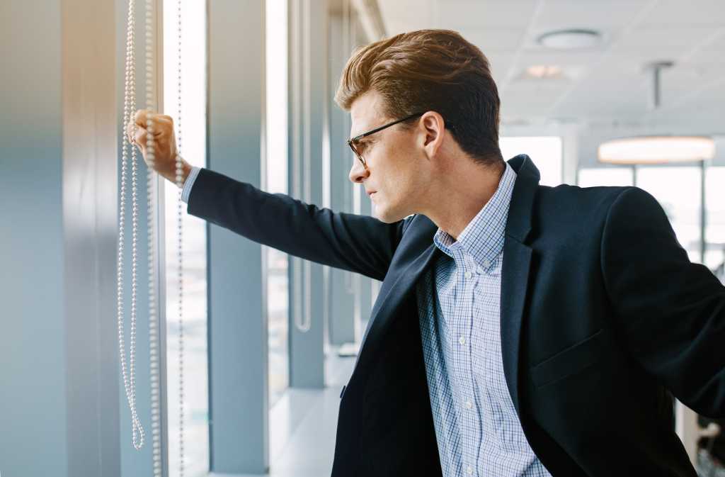 Side view shot of mature businessman standing in office. Caucasian male executive standing by window and looking outside.