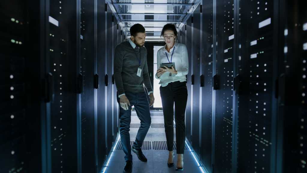 Male and Female Server Technicians Working in Data Center. Running Rack Server Diagnostics. Woman Uses Tablet Computer.