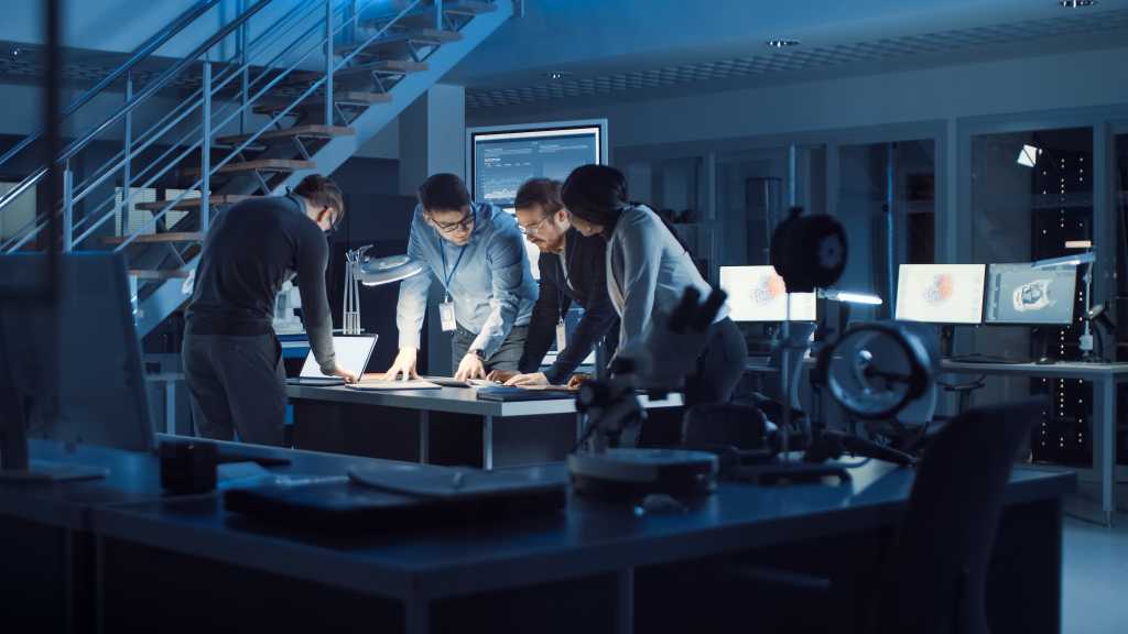 Diverse Team of Electronics Development Engineers Standing at the Desk Working with Documents, Solving Project Problems Late at Night. Specialists Working on Ultra Modern Industrial Design.