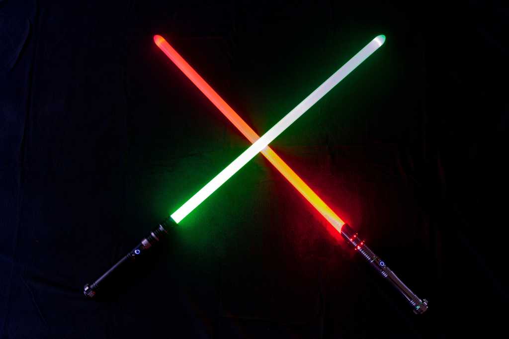 Two glowing crossed light saber laser sword blades with green color and red color against black background